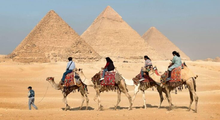 four people riding on camels across the pyramids